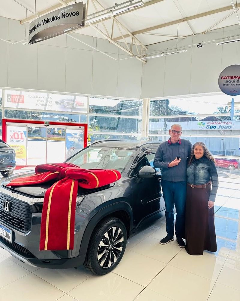 Casal ao lado do Honda WR-V novo, com laço vermelho, na concessionária